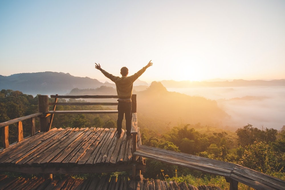 Man rising his hands and standing alone enjoying the sunrise