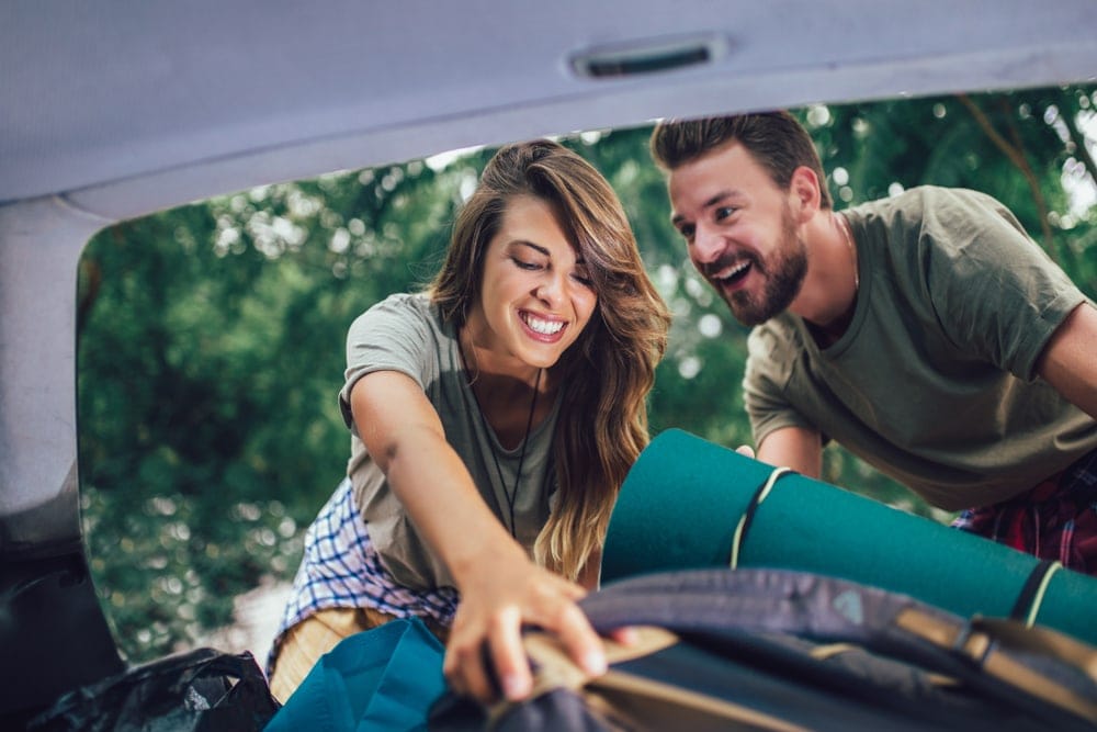 Couple unpacking camping gears from car trunk