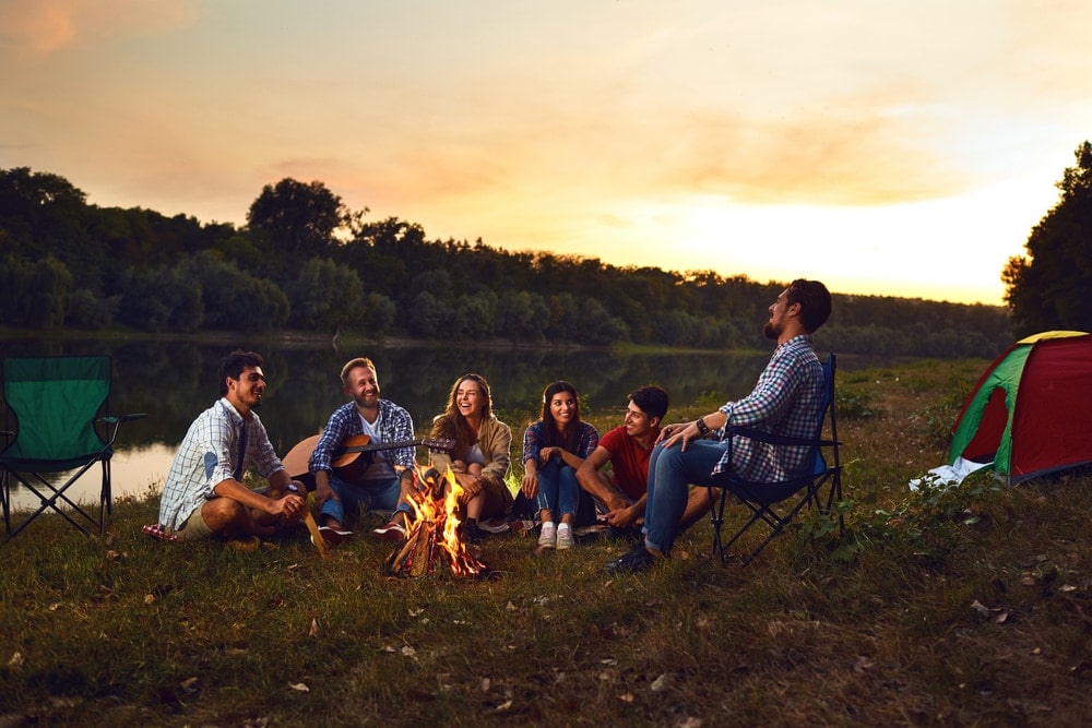 Group of friends chatting and smiling with a campfire beside