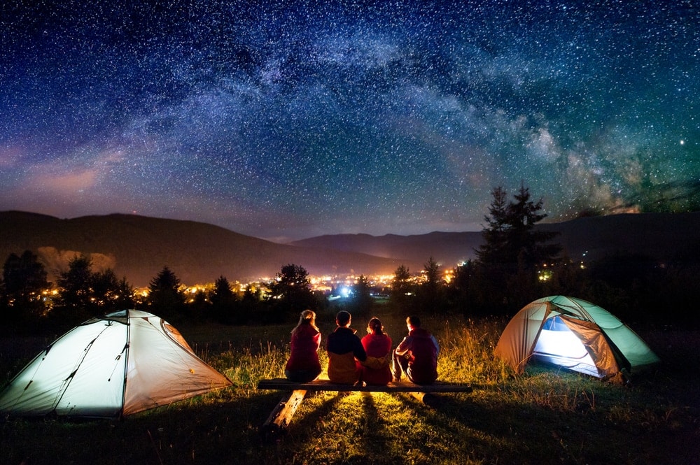 Group of friends camping under starry night with city lights view