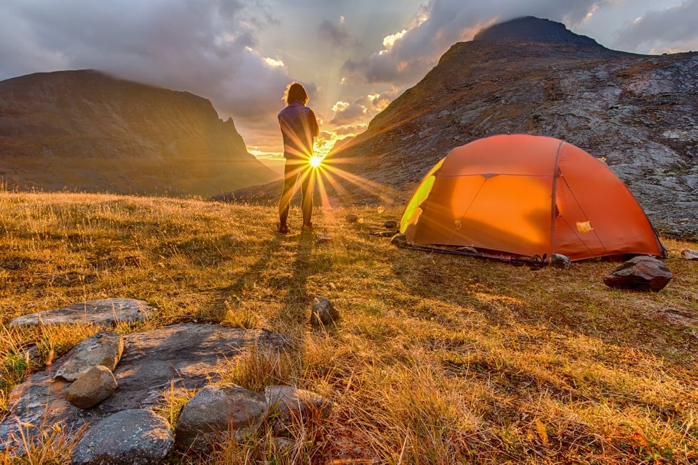 A man looking at the sun with camping tent beside