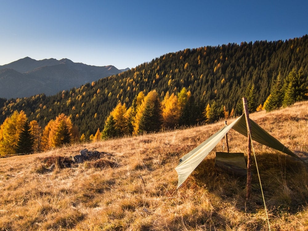 A simple tarp shelter on a hill with autumn trees in the background