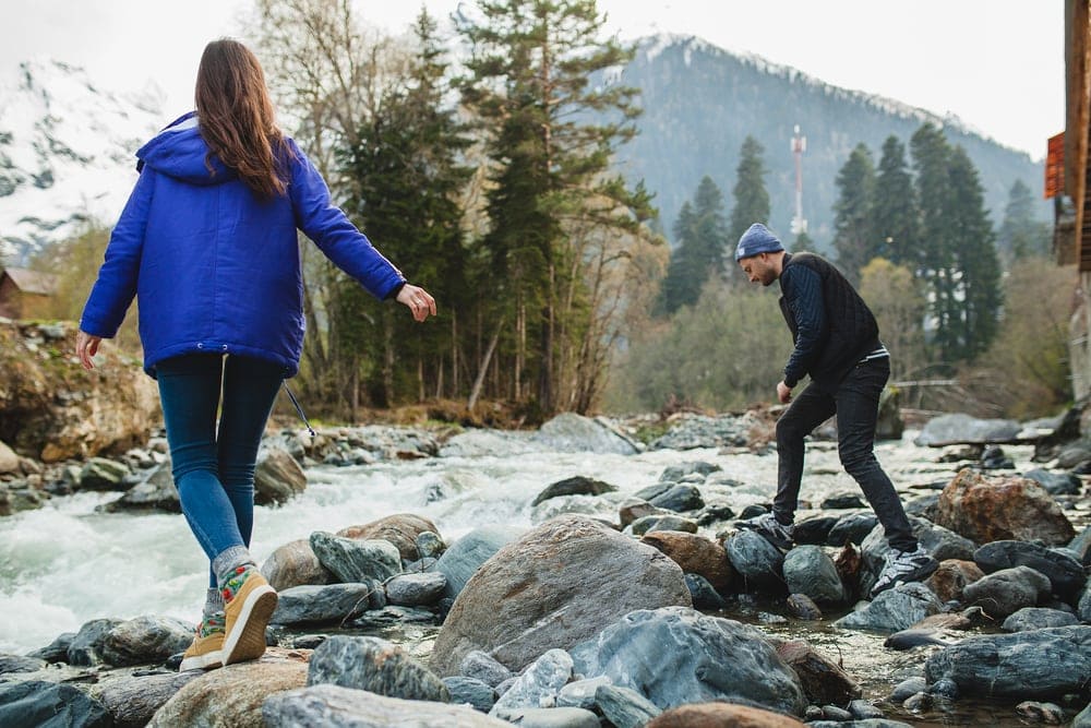 Beautiful couple hiking on rocks at river in winter forest