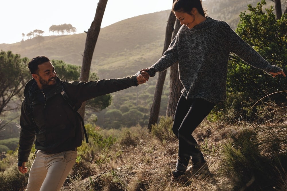 Guy helping his girlfriend walking down the mountain trail