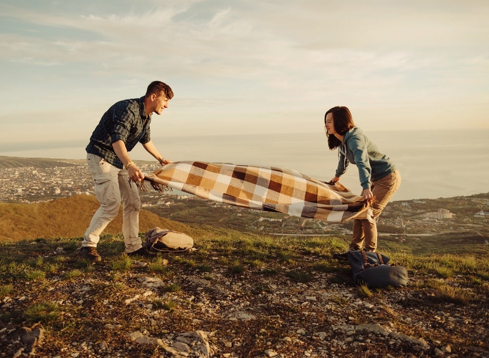 Couple spreading a blanket on a hill after hiking