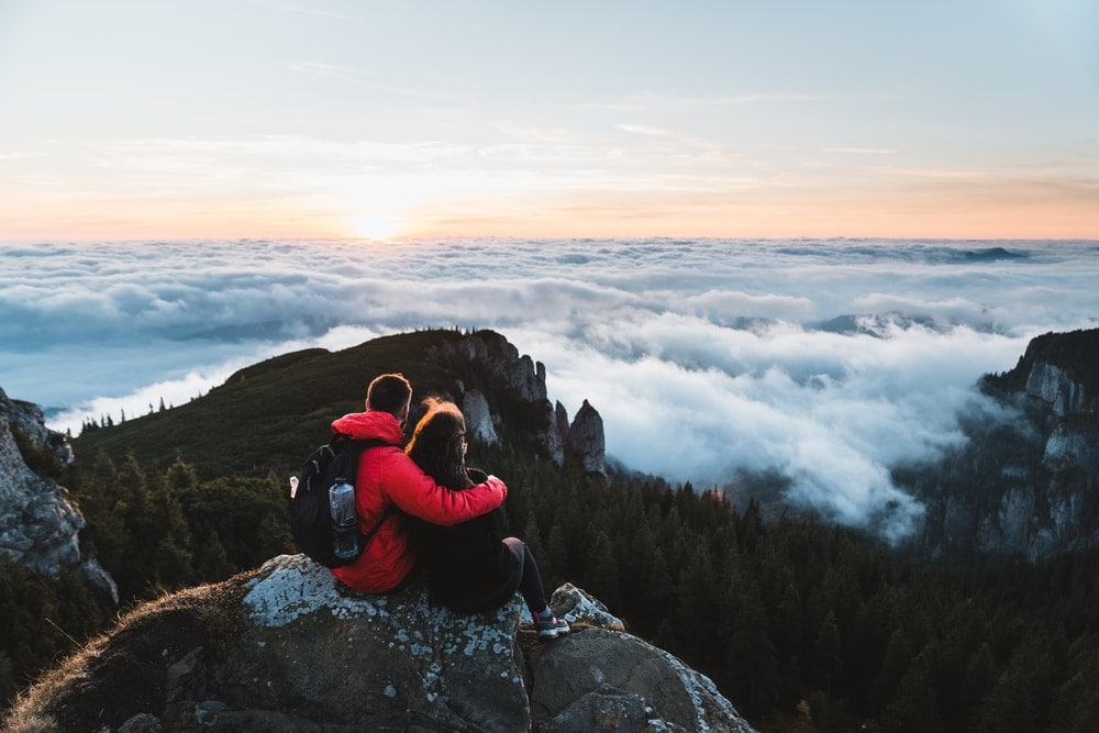 Couple on top of the mountain watching together the sea of clouds after hiking