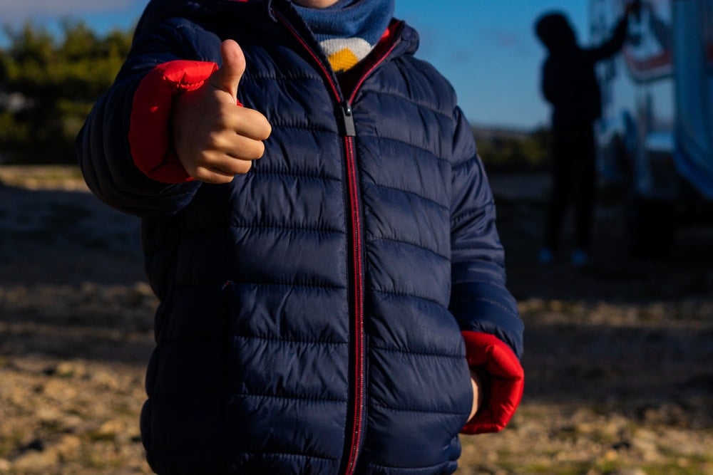 A man wearing a blue outdoor jacket making thumbs up gesture