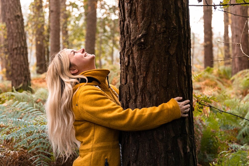 Woman wearing a fleece jacket hugging a tree in the woods