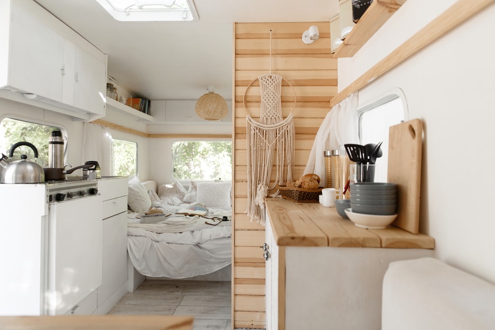 inside of a RV Camper with a cozy bed, tables and mini kitchen