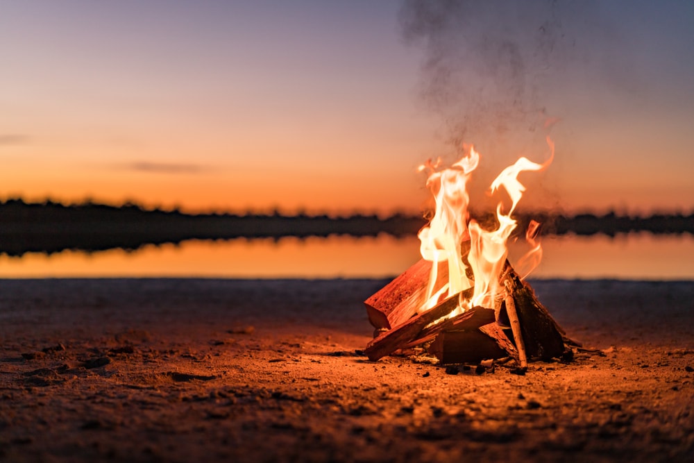 a small campfire by the lake during sunset