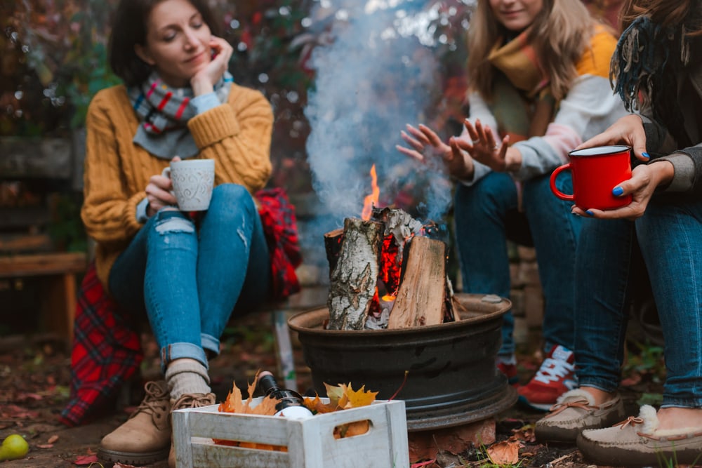 friends relaxing and drinking while warming themselves by a campfire in the wilderness