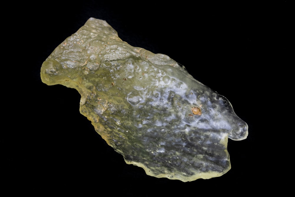 The Libyan desert glass specimen showing its yellow to translucent hue on a black backfournd