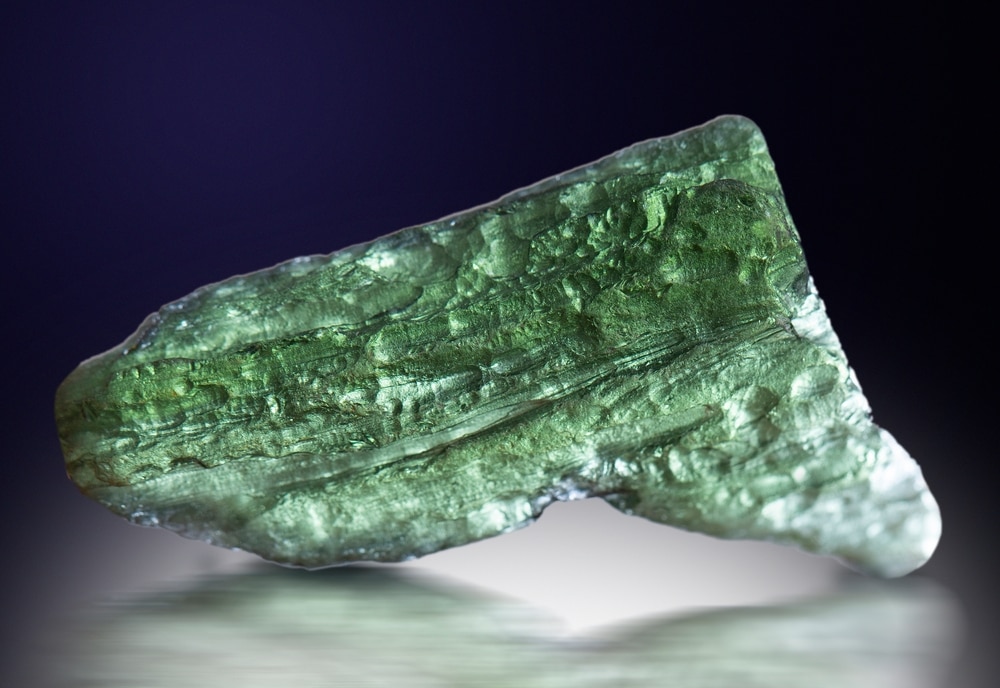 a moldavite gem stone specimen on a black background showings its olive green hue