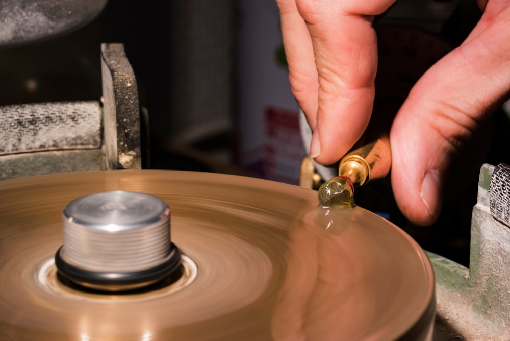 Craftsman cutting and polishing a green gemstone on a turning metal lap.