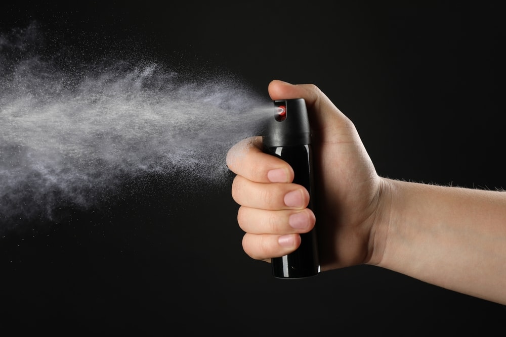 man using a pepper spray isolated on a black background