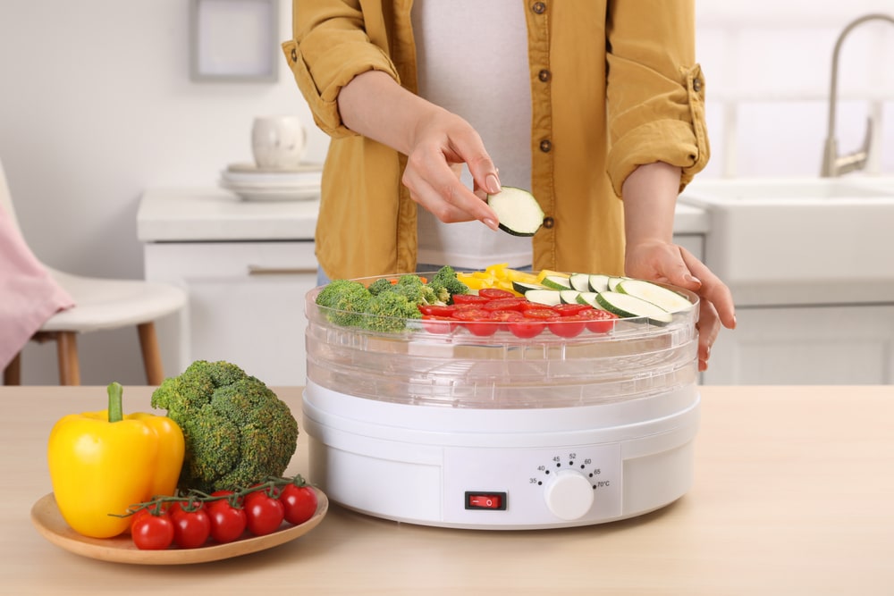 A woman putting cut vegetables  in a dehydrator machine