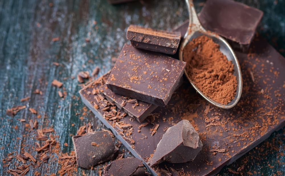 Dark Chocolate on a wooden table with spoon of dark chocolate powder as well