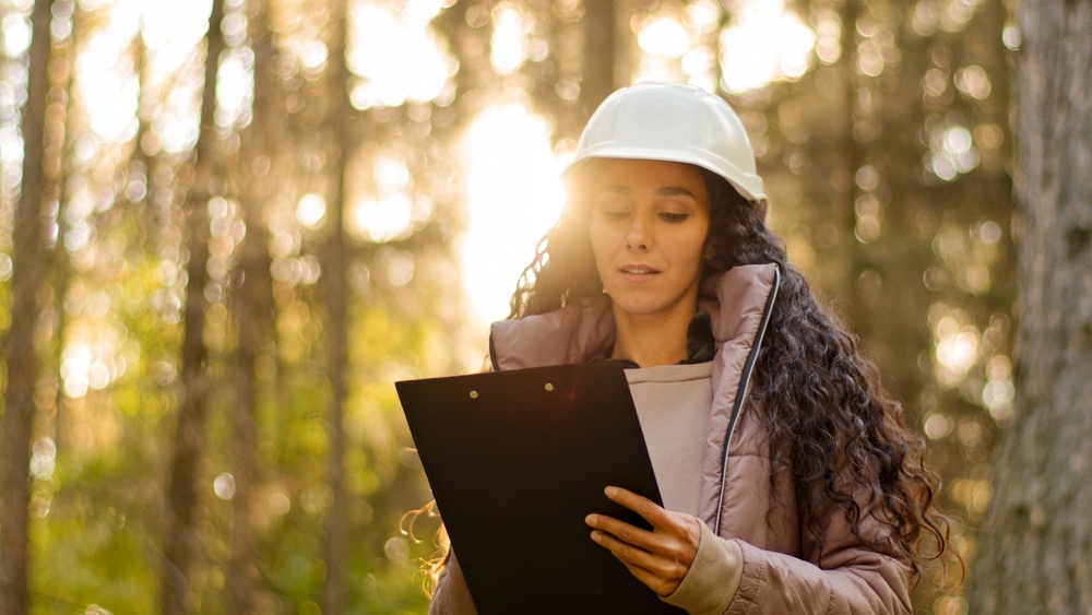 A woman wearing a hard hat inspecting as forest 