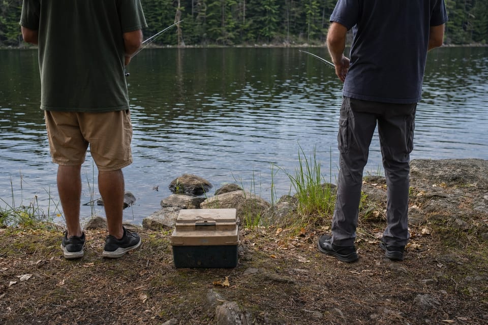 Two people fishing from a quiet lakeshore at dawn